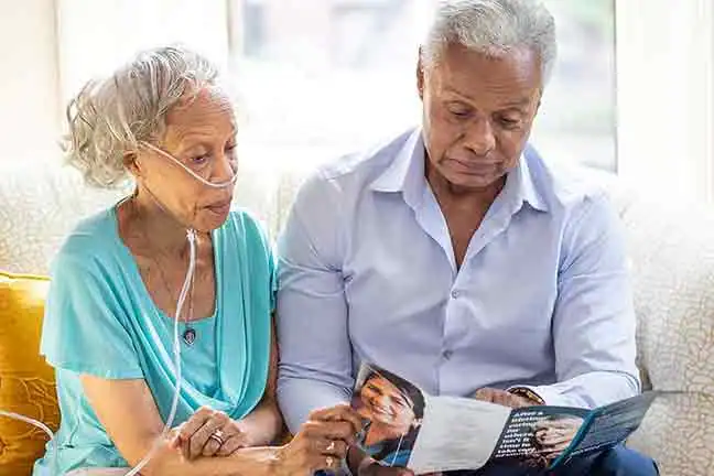 senior-woman-with-oxygen-and-senior-man-sitting-on-couch-reading-brochure